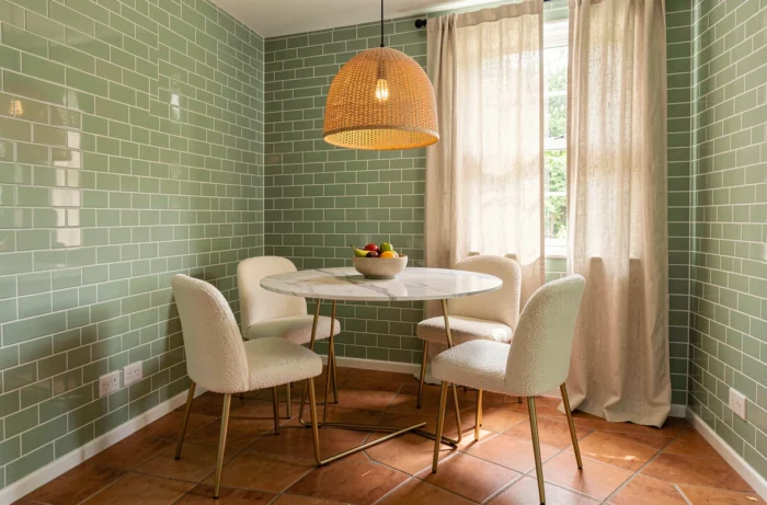 Coin repas de cuisine réaménagé avec table en marbre, chaises en bouclé blanc cassé et carrelage métro vert sauge pour une déco intérieure tendance