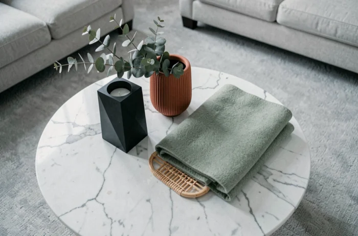 Flat lay d'accessoires décoratifs CallMeSpring sur une table basse en marbre : bougeoir géométrique, vase en terre cuite et plaid en laine sauge